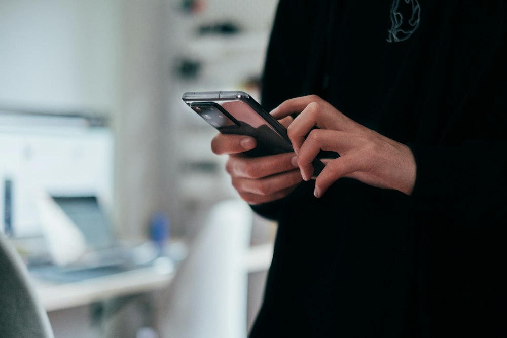 Person typing a message on a phone beside a laptop